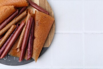 Delicious fruit leather rolls on white tiled table, top view. Space for text