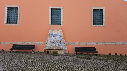 Traditional Portuguese Tile Fountain on Pink Wall with Two Benches and Cobblestone Ground