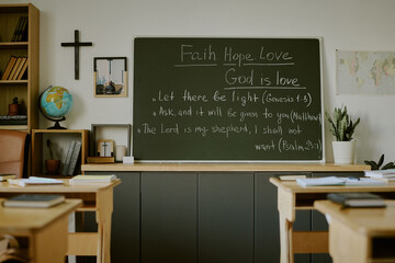 Classroom showcasing blackboard with religious quotes, wooden desks, books, and cross. Suitable for...