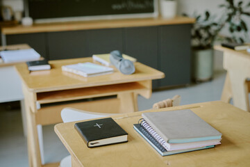 Neatly arranged books and closed notebooks on empty classroom desks with chalkboard and other educational supplies in background, creating atmosphere of anticipation for learning
