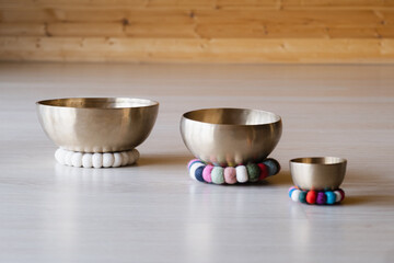 Three singing bowls of various sizes rest on colorful felt cushions on a light wooden floor. Perfect for meditation, sound therapy, and harmonious interiors