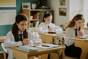 Students sitting at their desks in classroom diligently studying religion with books, notebooks, and stationery neatly arranged