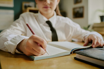 Unrecognizable schoolgirl holding pencil and writing in open notebook on desk