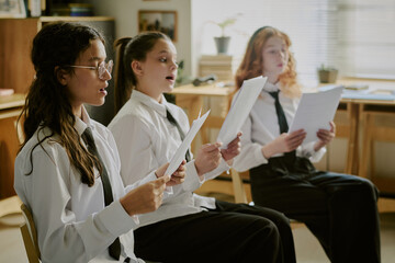 Group of students engaging in singing practice while holding sheets of paper in a music classroom...