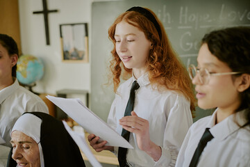 Group of students and nun engaged in academic presentation, with cross and blackboard in background, sharing knowledge in structured environment