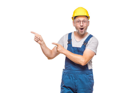 Surprised middle-aged construction worker while standing and pointing to blank space - copy space, promoter repairman with happy laugh, isolated on white background. Craftsman against white wall