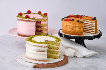 Pistachio, Medovik Honey Layer Cake, and Raspberry Cakes and slice with napkin Rose Butter cream, pink and white frosting side view of elegant desserts