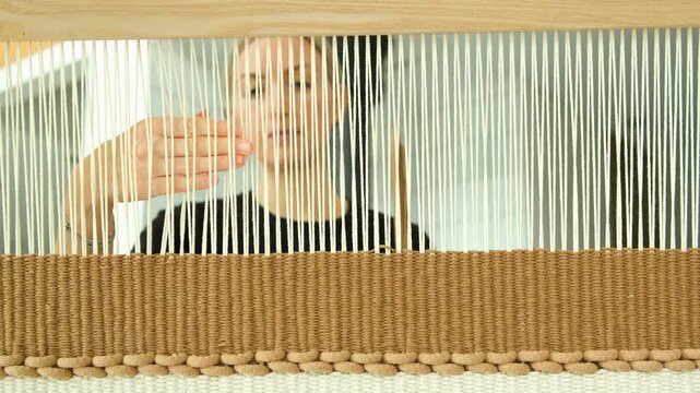 Mid age woman making traditional hand weaving tapestry on wooden weaving loom. Woman working on weaving loom using craft weaving technique