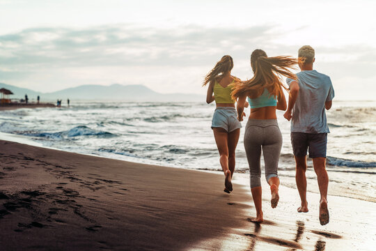 Group running on beach jogging having fun training. Exercising runners training outdoors