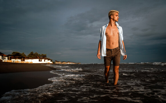 Adult young handsome fit man in white shirt at the beach enjoying calm, relaxation and mindfulness.