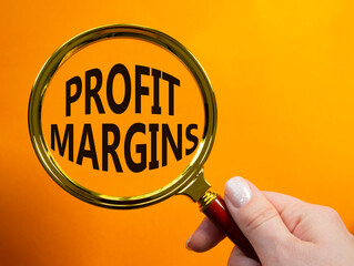 Profit Margins symbol. Magnifying glass with words Profit Margins. Beautiful orange background....