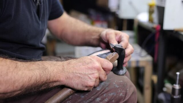 Hands of man fixing leather with nails and needles on the sole of a boot while working on new shoes.