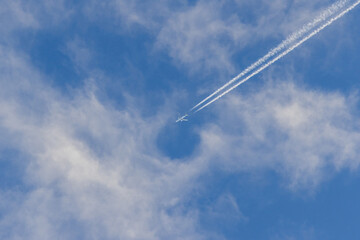 White airplane flying at high altitude leaving contrail in the blue sky