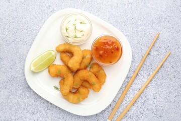 Tasty tempura shrimps, lime, sauces and chopsticks on grey textured table, flat lay