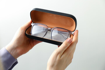 Woman holding case with stylish glasses and cleaning cloth on light background, closeup