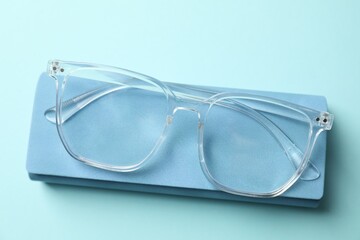 Case with stylish glasses on light blue background, top view