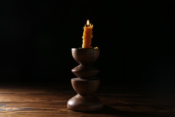Burning candle in candlestick on wooden table in darkness