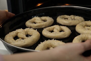 Woman putting baking dish with uncooked pretzels into oven, closeup