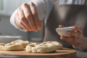 Woman adding sea salt onto uncooked pretzels at table indoors, closeup