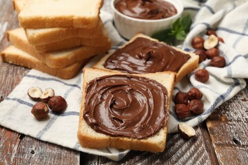 Toasts with chocolate hazelnut spread, nuts and mint on wooden table, closeup