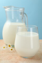 Fresh milk and flowers on table against light blue background, closeup