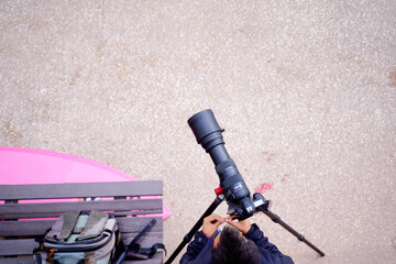 Aerial view of a person holding a camera on a tripod, capturing images. The ground is textured with...