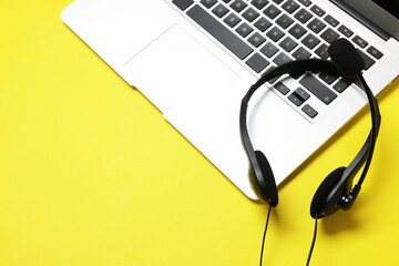 Headset with microphone and laptop on yellow background, above view. Space for text