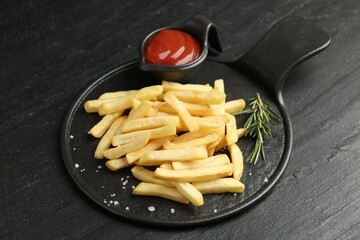 Tasty french fries served with ketchup and rosemary on black table, closeup
