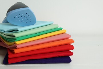 Upright steamer and stack of folded clothes on white wooden table, closeup. Space for text