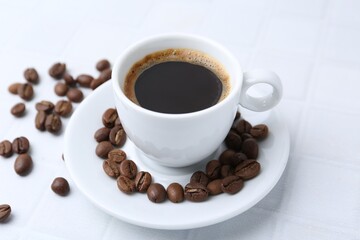 Aromatic coffee in cup and beans on white table, closeup