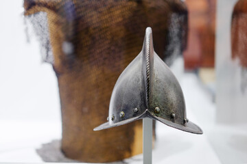 A medieval helmet on display in a museum, with chainmail armor in the background.
