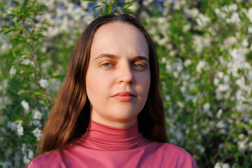 Fototapeta premium Young woman's portrait with blurred flowering trees in the background. Spring beauty and nature setting.