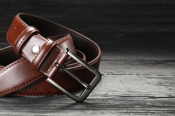 One brown leather belt on wooden table, closeup. Space for text