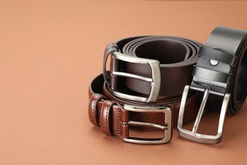 Three leather belts on pale brown background, closeup. Space for text