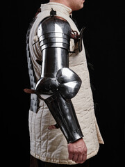 A side view of a medieval steel arm armor worn over a padded garment, showcasing its design and...