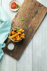 Home style french fries in a blue bowl with ketchup and ranch dressing for dipping, on a rustic cutting board. Vertical.