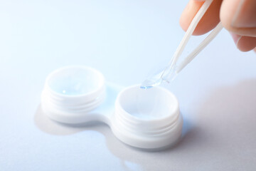 Woman taking contact lens out of case with tweezers on white background, closeup
