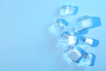 Cubes of clear ice on light blue background, flat lay. Space for text