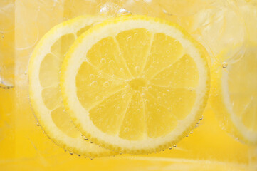 Refreshing soda water with slices of lemon and ice in glass on yellow background, closeup