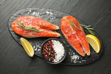 Seafood. Salmon steaks, spices and lemon wedges on black textured table, top view