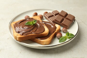 Toasts with tasty chocolate spread, pieces, mint and hazelnuts on light table, closeup
