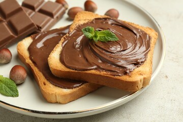 Toasts with tasty chocolate spread, pieces, mint and hazelnuts on light table, closeup