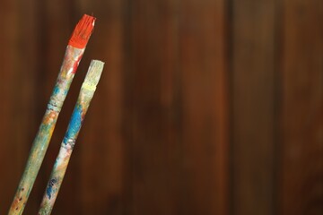 Two dirty paintbrushes on wooden background, closeup. Space for text