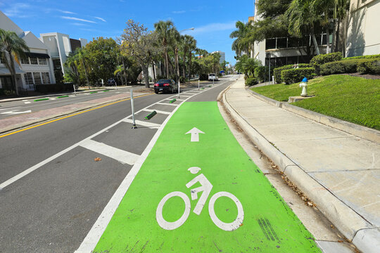 Cycling lane painted green stretches through Sarasota city road with moving cars. Florida urban bike-friendly street