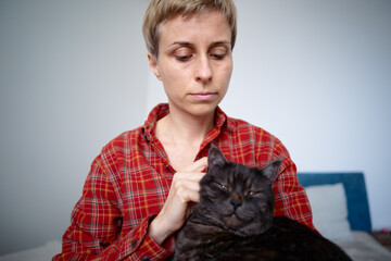 Woman in Red Plaid Shirt Holding a Relaxed Black Cat Indoors..