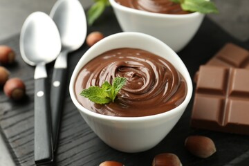 Tasty chocolate spread, pieces, mint and hazelnuts on table, closeup
