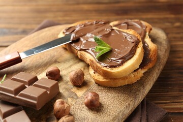 Toasts with tasty chocolate spread, pieces, mint and hazelnuts on table, closeup