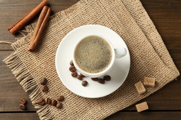 Aromatic coffee in cup, beans, brown sugar and cinnamon on wooden table, flat lay