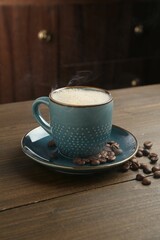 Aromatic coffee in cup and beans on wooden table, closeup