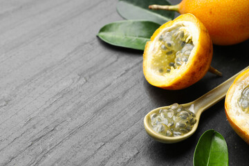 Ripe passion fruits, seeds and green leaves on black table, closeup. Space for text